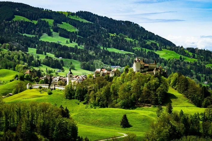 Majestic view of Gruyères Castle in the Swiss Alps, perched on a hilltop with stunning alpine scenery, featuring its medieval architecture, stone walls, and beautiful surrounding landscapes of rolling hills and mountains.